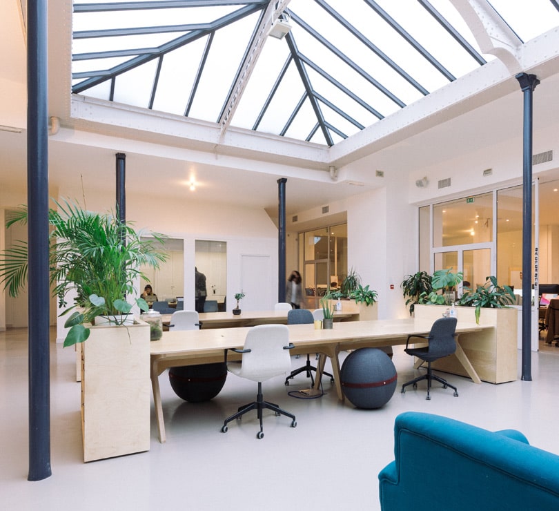 aménagement des bureaux d'atomic digital design à Paris avec des grandes tables en bois, des casiers de rangement, des sièges de bureau et une verrière