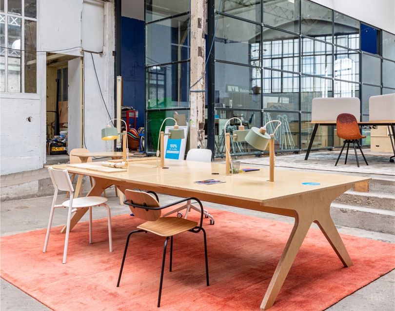 Grande table de bureau sur mesure en bois clair avec des lampes, des chaises design et un tapis orange