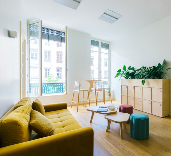 un coin salon dans un bureau professionnel avec un canapté jaune, des poufs, une table basse gigogne et un rangement en bois