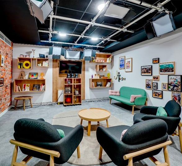 espace détente en entreprise avec de grand fauteuils noirs, une table basse et un mur décoré avec de nombreaux cadres et tableaux