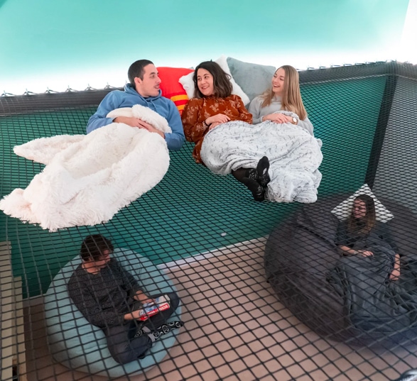 quatre personnes se détendent dans un espace cosy sur des filets suspendus et des poufs