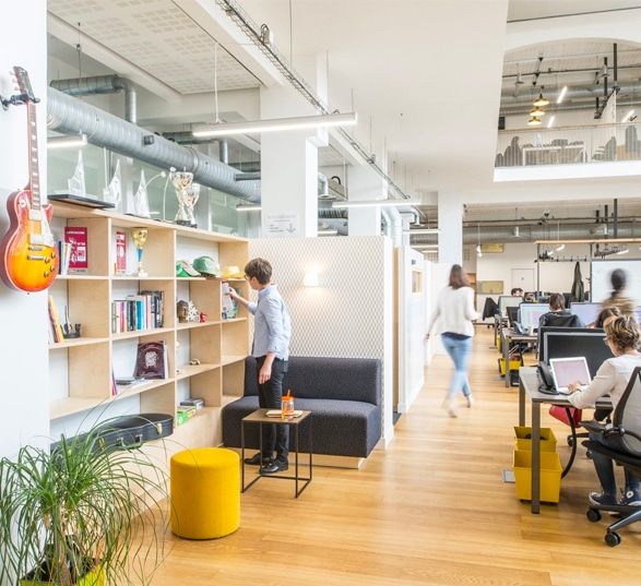 open space avec bureaux, plantes, guitare et des personnes qui travaillent