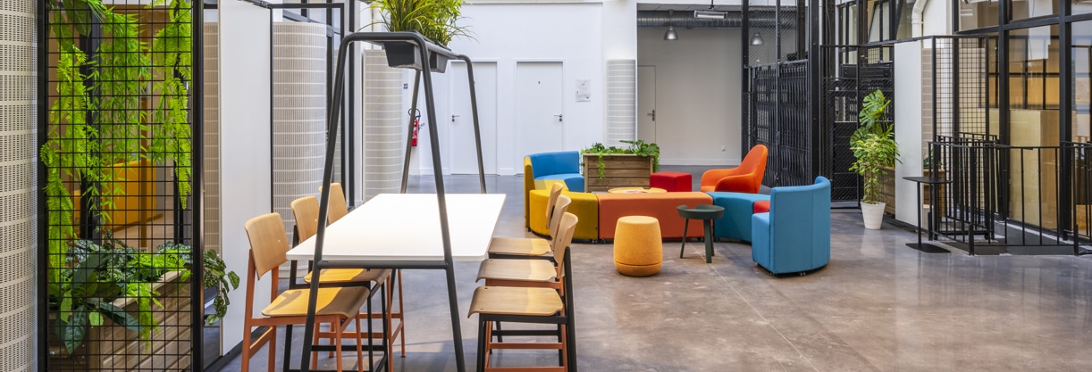 Espace de collaboration en entreprise avec une table en bois, un canapés colorés et des plantes vertes.