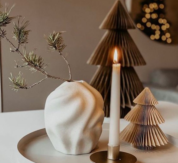 Décorations de Noël minimalistes avec un deux sapins en carton, un vase design blanc et une bougie. 