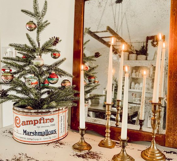 Décoration de Noël vintage avec un miroir, des vieux bougeoirs et un petit sapin de Noël dans une conserve vintage.