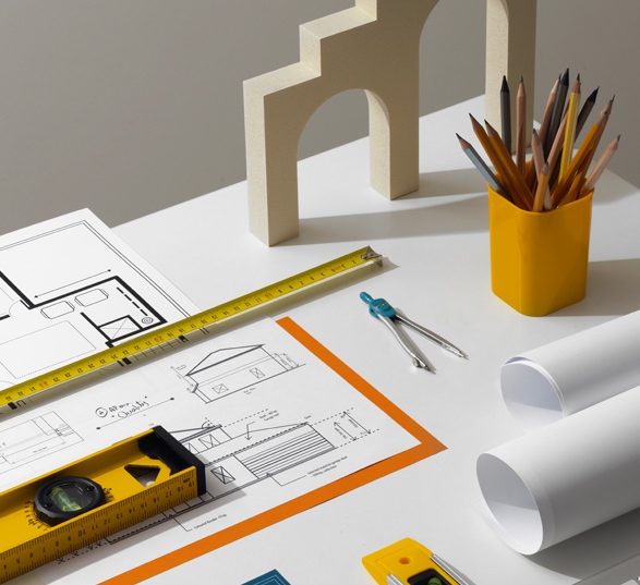 Plateau de travail avec un plan sur papier, des stylos et crayons, un mètre et un laser. 