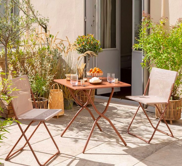 Terrasse aménagé avec une table et deux chaises et des plantes vertes

