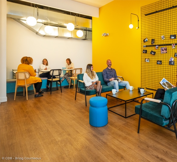 Espace de travail collaboratif en entreprise avec des murs jaunes, des tables et des chaises.