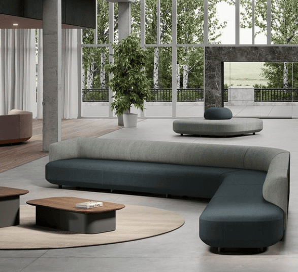 Espace informel en entreprise avec un canapé d'angle gris, des tables basses, de grandes baies vitrées et des plantes.
