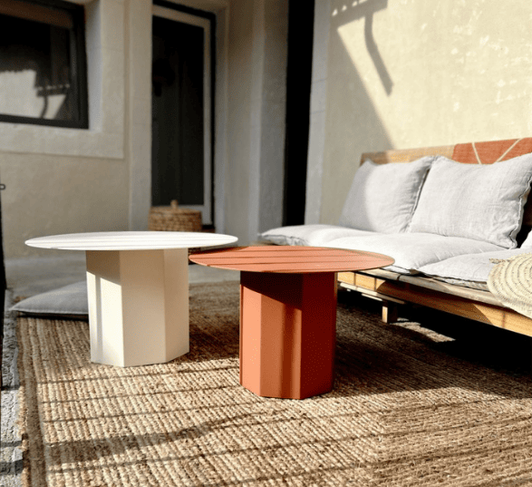 2 tables de basse ronde, blanche et rouge avec un tapis en rotin et une banquette avec des coussins gris