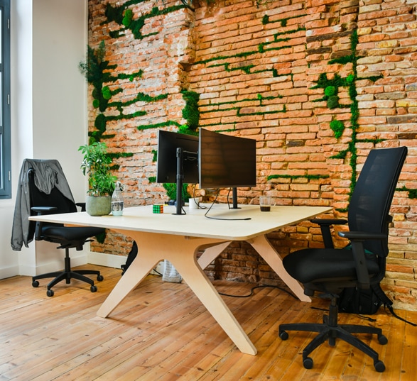 Bureau collaboratif, bench, en bois clair et un mur en pierres
